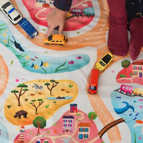 Mains d'enfant qui jouent aux petites voitures sur les routes de l'imprimé Croisée des mondes, gros plan