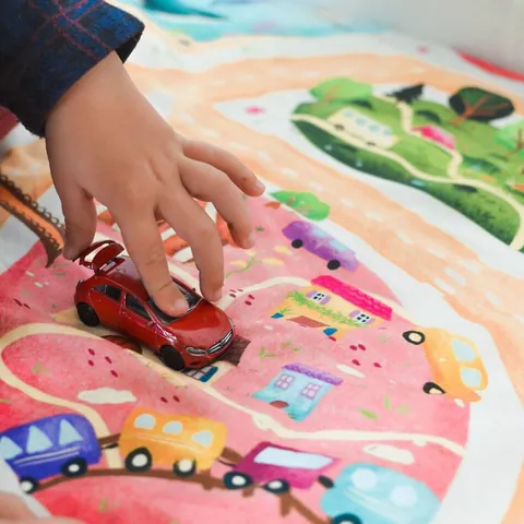 Main d'enfant qui fait rouler une voiture rouge sur l'imprimé Croisée des mondes, gros plan