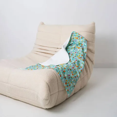 Couverture vert d'eau à fruits drapée sur un fauteuil bas en bouclette écrue