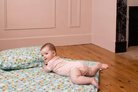 Bébé en body rose sur le ventre devant l'oreiller Pique-nique, tapis assorti, chambre aux murs roses
