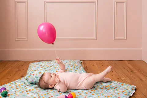Bébé allongé la tête sur l'oreiller Pique-nique qui regarde un ballon rose, chambre aux murs roses