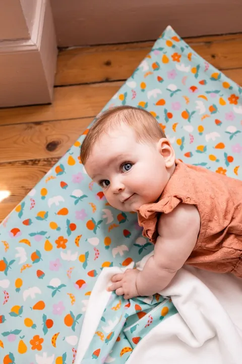 Bébé qui regarde l'objectif, la main sur la couverture Pique-nique repliée qui montre son molleton blanc
