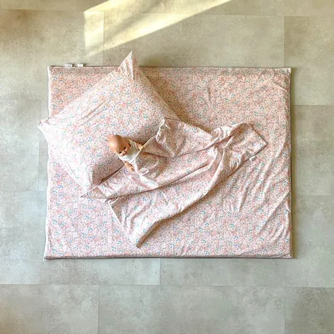 Poupon sur le tapis rose poudré à petites fleurs avec l'oreiller et la couverture assortis, vue de dessus