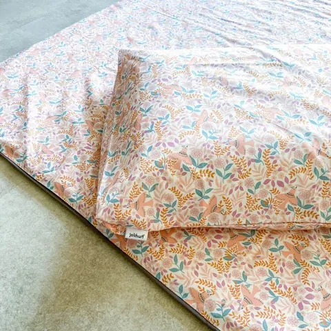 Oreiller housse rose poudré à petites fleurs posé sur le tapis assorti, étiquette Jolihuit