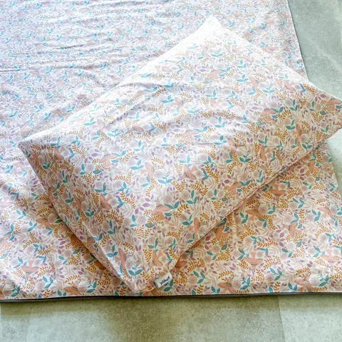 Oreiller rose poudré à petites fleurs posé de biais sur le tapis assorti, gros plan