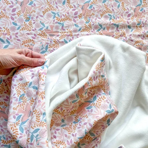 Main qui ouvre la couverture rose poudré à petites fleurs sur sa doublure blanche, gros plan