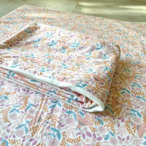 Couverture rose poudré à petites fleurs pliée en rouleau, doublure blanche visible
