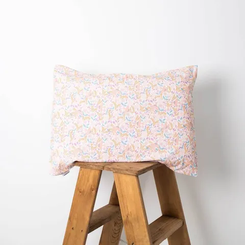 Oreiller housse rose poudré à petites fleurs posé sur un tabouret en bois, fond blanc