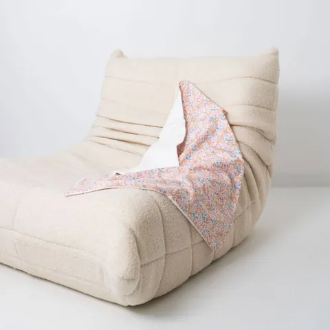Couverture poésie drapée sur un fauteuil bas en bouclette écrue, fond blanc