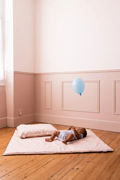Bébé allongé sur le tapis Poésie, oreiller Poésie en tête de tapis, ballon bleu, plan large de la chambre rose
