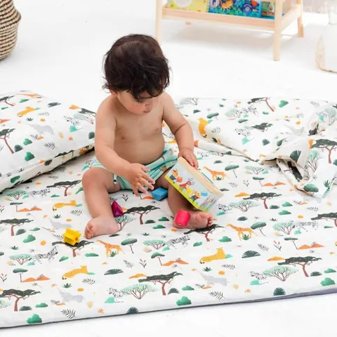 Bébé qui joue assis sur le tapis savane, oreiller et couverture assortis autour de lui, plan rapproché