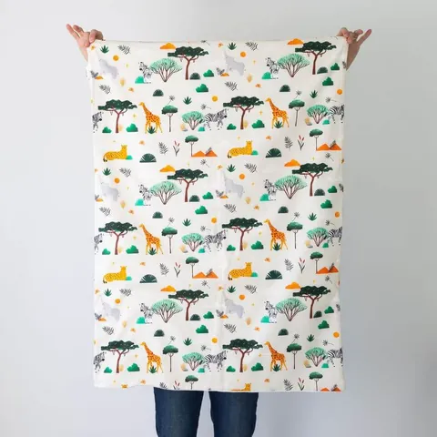 Couverture savane dépliée, tenue à bout de bras devant un mur blanc