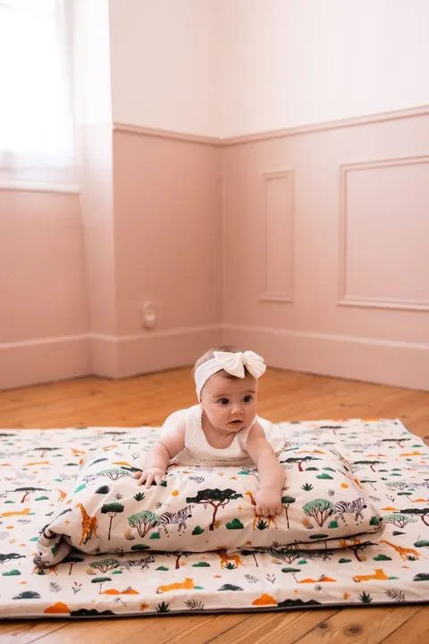 Bébé assis derrière l'oreiller Savane posé sur le tapis assorti, plan large de la chambre rose