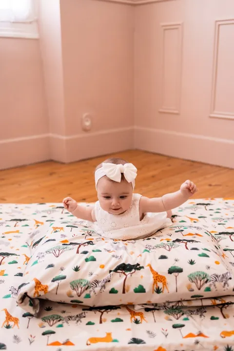 Bébé qui s'appuie bras écartés sur l'oreiller Savane, tapis assorti, chambre rose