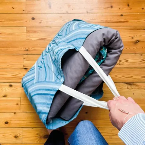 Mains qui glissent un tapis roulé dans le sac cabas bleu tissé, parquet
