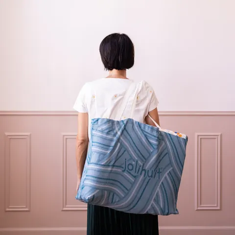 Femme de dos qui porte le sac cabas bleu tissé, cadrage serré, chambre rose