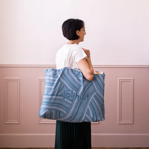 Femme de dos qui porte le sac cabas bleu tissé Jolihuit à l'épaule, chambre rose moulurée