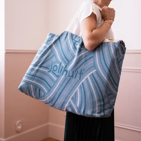 Sac cabas bleu tissé Jolihuit porté à l'épaule, chambre rose moulurée, visage hors cadre