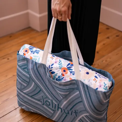 Sac cabas bleu tissé tenu à la main, tapis Bouquet printanier plié dedans, parquet