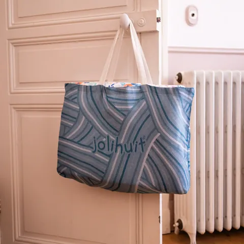 Sac cabas bleu tissé Jolihuit suspendu à une porte moulurée, radiateur en fonte