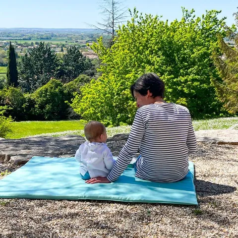 Une mère et son bébé assis de dos sur le Tapis Magique Le baroudeur, face à la vallée