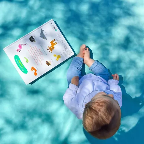 Bébé vu du dessus, assis près d'un imagier sur le coton turquoise du Tapis Magique Le baroudeur