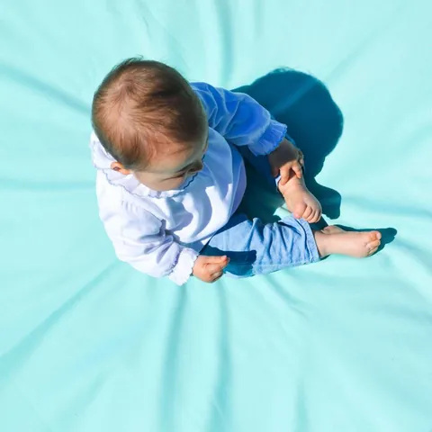 Bébé vu du dessus assis sur le tapis Baroudeur turquoise