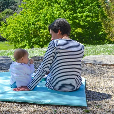 Mère et bébé assis sur le tapis Baroudeur, jardin verdoyant en fond