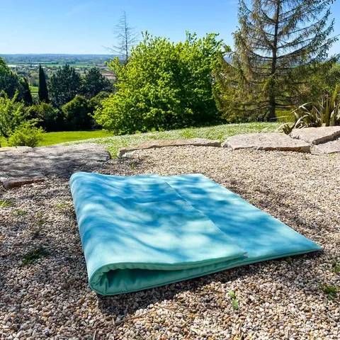 Tapis Baroudeur plié en deux sur le gravier d'un jardin, vallée et arbres en fond