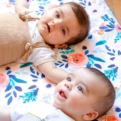 Deux bébés allongés tête contre tête sur le tapis Bouquet, regards vers l'objectif
