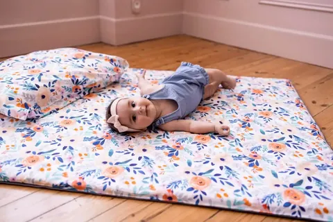 Bébé allongé sur le tapis blanc à fleurs orange et bleues avec coussin assorti, parquet, plan rapproché au ras du sol