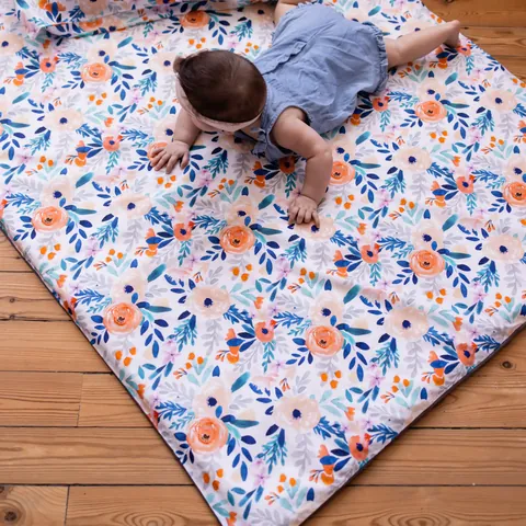 Bébé à quatre pattes sur le tapis blanc à fleurs orange et bleues posé en biais sur un parquet, vue de dessus, tapis entier
