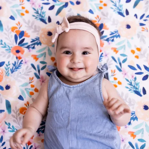 Bébé souriant au bandeau rose, allongé sur le Tapis Magique Bouquet printanier