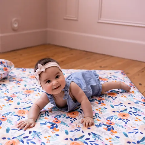 Bébé souriant à quatre pattes sur le tapis Bouquet, parquet et murs roses