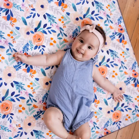 Bébé souriant allongé sur le dos, bras ouverts, sur le tapis Bouquet, vue du dessus