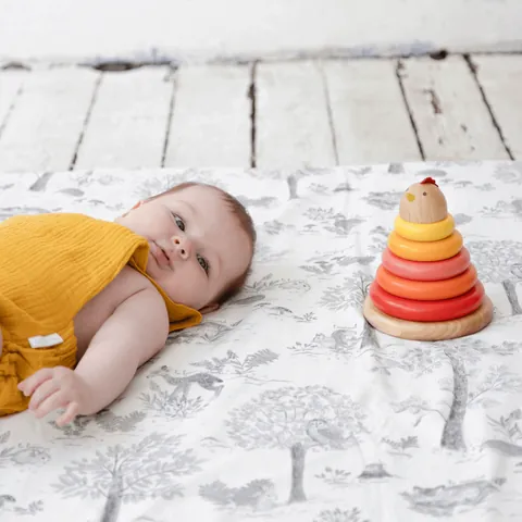 Bébé en haut moutarde allongé sur le tapis Doux sous-bois à côté d'une pyramide à empiler