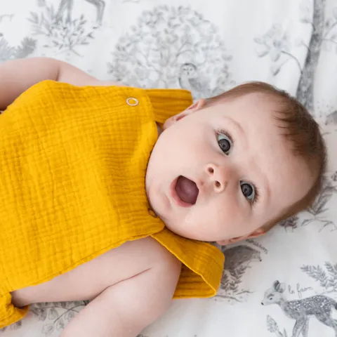 Gros plan d'un bébé étonné, bouche ouverte, allongé sur l'imprimé Doux sous-bois