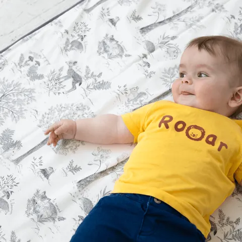Bébé souriant allongé sur le tapis blanc à dessins gris de sous-bois, imprimé bien lisible, vue plongeante