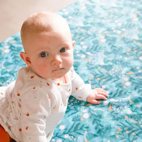 Bébé aux yeux bleus appuyé sur les bras sur le tapis Forêt magique, regard vers l'objectif