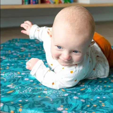 Bébé souriant sur le ventre sur le tapis Forêt magique, étagère en fond