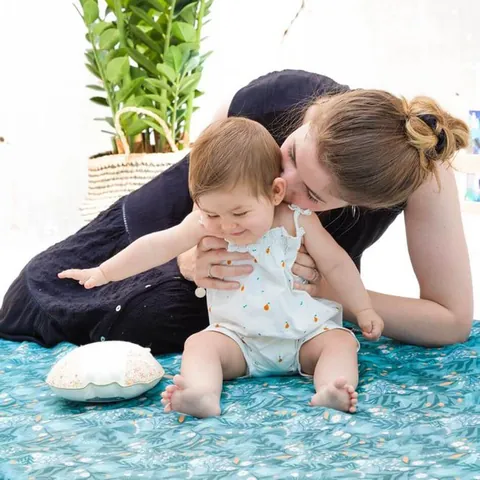 Femme qui embrasse un bébé qui rit, assis sur le tapis vert d'eau à feuillages