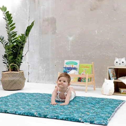 Bébé sur le ventre sur le tapis Forêt magique, mur de béton, plante, présentoir de livres et veilleuse chat
