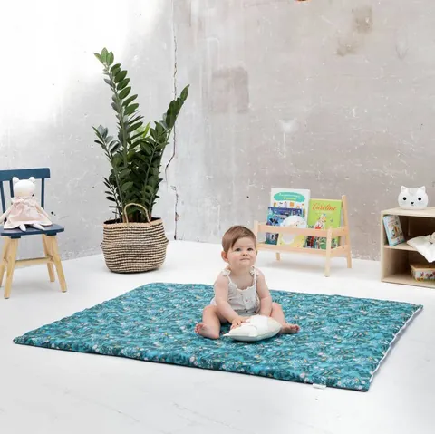 Bébé assis sur le tapis vert d'eau à feuillages avec un coussin, plan large