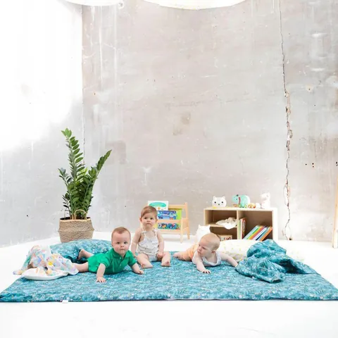 Trois bébés sur le tapis Forêt magique dans une pièce claire, plante et présentoir de livres