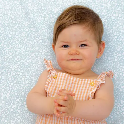 Bébé souriant en barboteuse à carreaux, allongé sur le Tapis Magique Gabi
