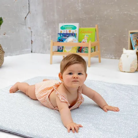 Bébé sur le ventre sur le tapis vert de gris à petites fleurs blanches, étagère à livres en fond