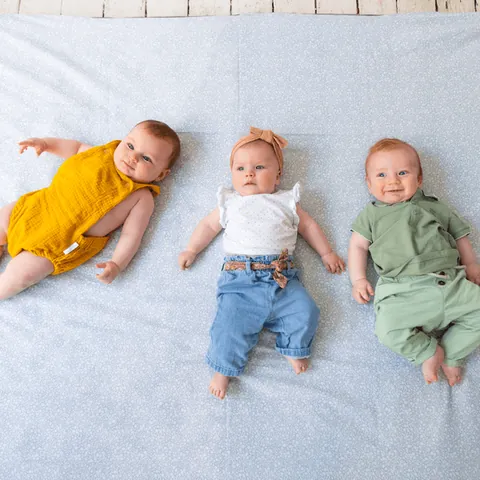 Trois bébés allongés côte à côte sur le tapis vert de gris à petites fleurs blanches, vue de dessus