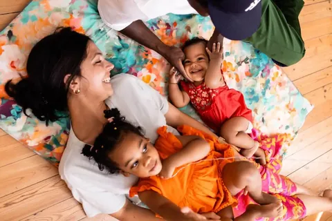 Famille allongée en rond sur le tapis à fleurs peintes turquoise et orange, deux enfants et un bébé, vue de dessus