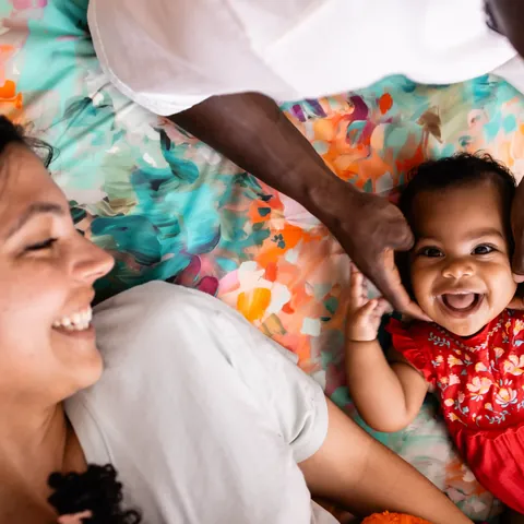 Bébé qui rit en robe rouge et sa mère souriante, allongés sur le tapis Jardin, cadrage serré