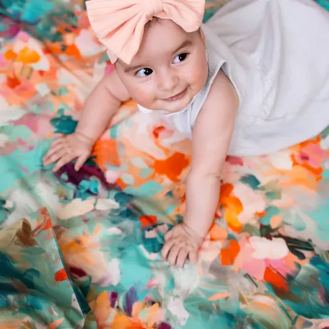 Bébé au nœud rose qui relève la tête sur le Tapis Magique Le jardin de l’artiste